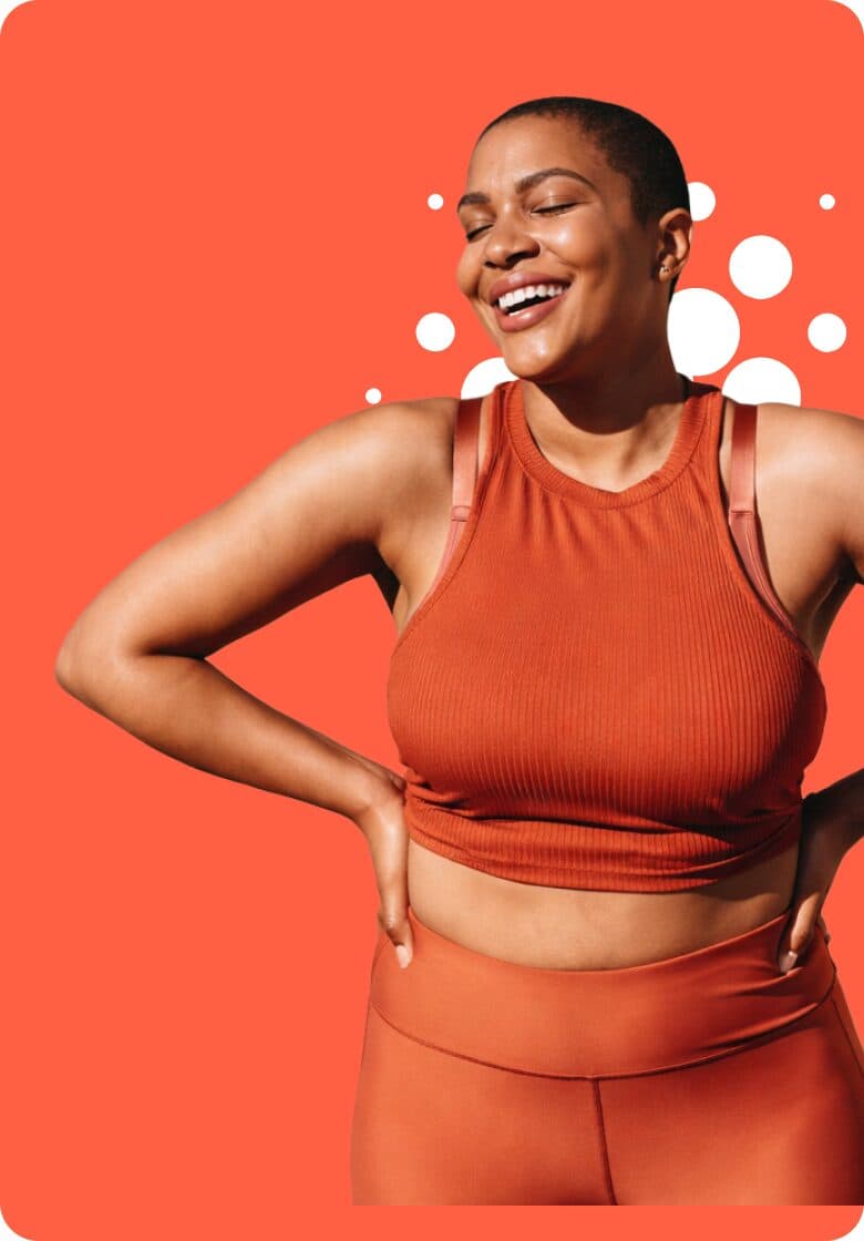 A smiling woman in burnt-orange athletic wear standing with her hands on her hips