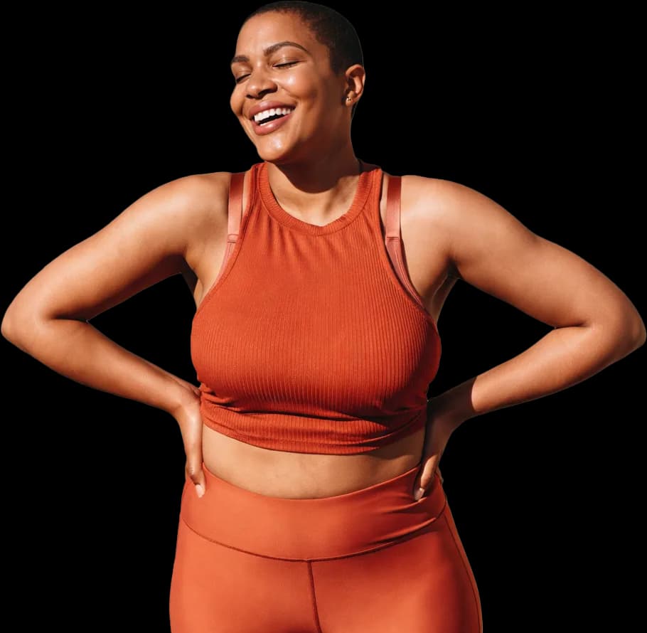 A smiling woman in burnt-orange athletic wear standing with her hands on her hips